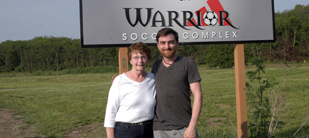 Carol Maas and Michael Blackwell standing in front of the Hank and Carol Maas Warrior Soccer Complex in Dayton Ohio